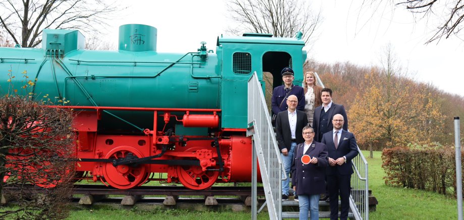 Die ausrangierte Lok im Aktivpark Phoenix weckt die Vorfreude auf den geplanten Pendelverkehr: untere Reihe (v. l.) Gudrun Rassat (Osnabrücker Förderkreis Eisenbahn-Tradition) und Bürgermeister Michael Gerdhenrich, Mitte: Uwe Denkert (Stadt Beckum) und Dr. Daniel Dierich (Energieversorgung Beckum), obere Reihe: Burkhard Rassat (Osnabrücker Förderkreis Eisenbahn-Tradition) und Marianne Witt-Stuhr (Stadt Beckum).